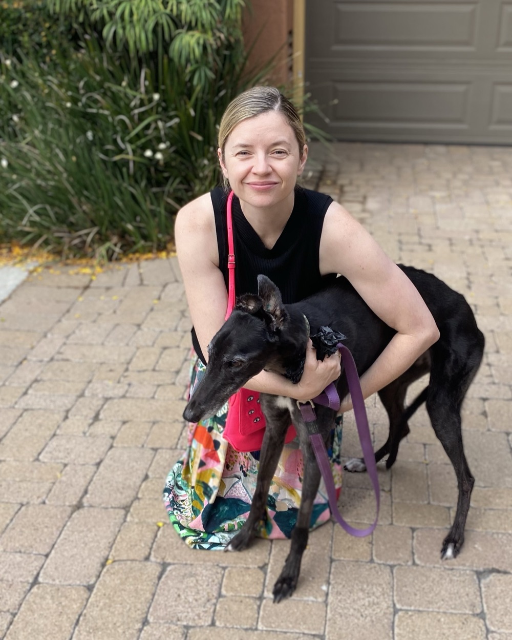 CC smiling, crouched beside her black dog